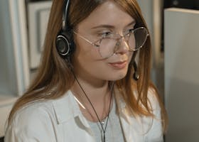A young woman with eyeglasses and headphones working in a call center.